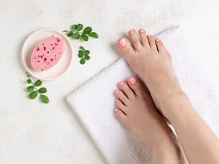 well-groomed female legs with a delicate pink pedicure on a white bath towel, organic rose soap and green leaves. Beauty, wellness and relaxation concept. White background. top view. close-up