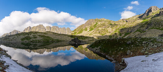 Fototapeta na wymiar Scenic view of mountains clouds and green with a reflection in a frogs lake. Stony shore. zabie pleso. frogs lake. High Tatras, Slovakia Concept of nature and tourism