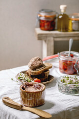 Ceramic bowl of homemade chicken liver pate with wooden knife, sliced rye bread, sun-dried tomatoes and green sprout salad on white linen table cloth. Home breakfast or appetizer