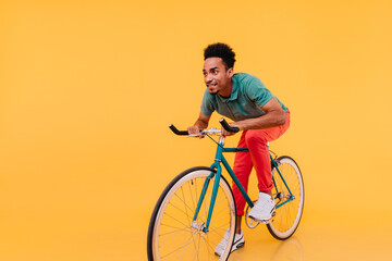Trendy african man in white sneakers posing emotionally on bike. Indoor portrait of enthusiastic...