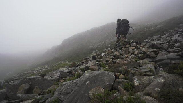 Man putting a stone on a cairn in the mountains with windy weather
