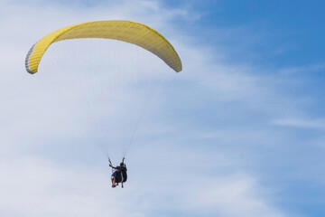 Two paragliders are flying in tandem against a blue sky. Copy space.