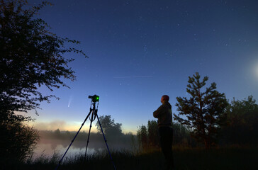 Ja i mój aparat na statywie podczas sesji fotograficznej komety C/2020 F3 NEOWISE, na brzegu jeziora o poranku - obrazy, fototapety, plakaty