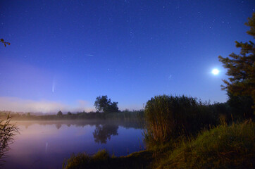 Kometa, gwiazdy, plejady, hiady, Wenus i Księżyc widoczne nad jeziorem o poranku