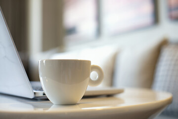 White coffee mug beside laptop computer for early morning work concept