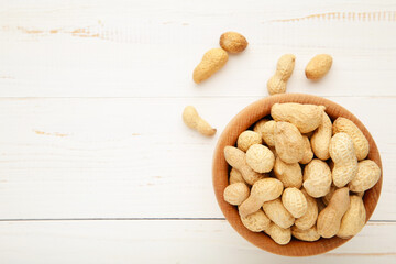 Dried peanuts in wooden bowl on white wooden background.