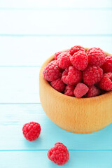 Ripe raspberries in wooden bowl on blue background. Top view