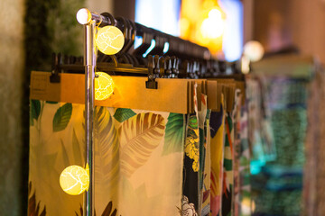 Vários cabides com amostras de tecidos em prateleira decorada com luzes .