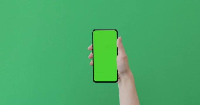 Young woman hand show smartphone with green screen on green background