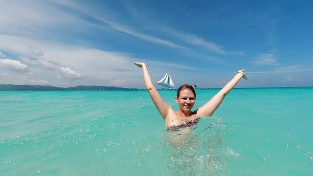 Young pretty smiling girl splashing sea waves with her hands. Having Fun in The Sea. Boracay, Philippines. Slow motion shot.