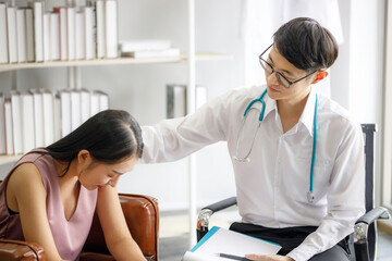 Asian male psychiatrist puts his hand on the shoulder of a young woman to give encouragement as she is worried by the spread of covid 19. Disease symptoms talk about health care concept