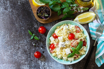Oriental cuisine. Healthy salad with couscous, tomatoes, feta cheese, basil, chili pepper and olive oil. Top view flat lay background. Copy space.