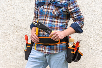A construction worker in a blue checked shirt holds a rivet tool in his hands.
