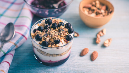 Homemade American dessert - yogurt with granola, jam and black currants in glass cups on a wooden blue table