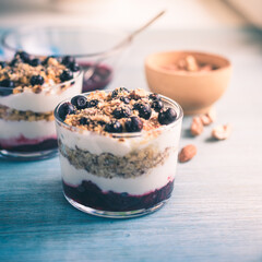 Homemade American dessert - yogurt with granola, jam and black currants in glass cups on a wooden blue table