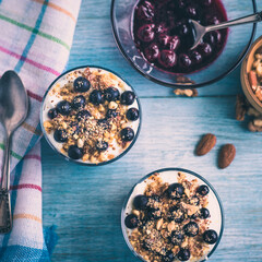 Homemade American dessert - yogurt with granola, jam and black currants in glass cups on a wooden blue table