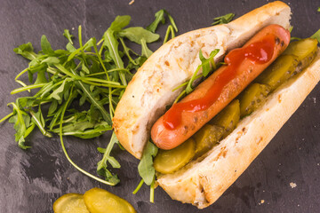 Cooking hot dogs - fried sausage with ketchup with sliced pickles and lettuce arugula to cut bun, close-up
