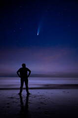 Watching comet NEOWISE high in the sky by a man on a beach during night