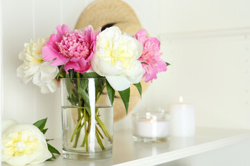 Bouquet of beautiful peonies in vase and candles on white table