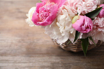 Beautiful peony bouquet in wicker basket on wooden table, closeup. Space for text