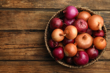 Onion bulbs in basket on wooden table, top view. Space for text