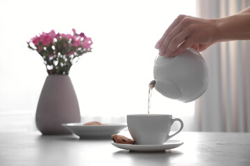 Woman pouring hot tea into cup at table, closeup