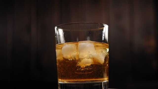 Close-up of a misted-up glass of whiskey with ice slowly spinning around on a wooden background. The concept of the celebration and alcohol.