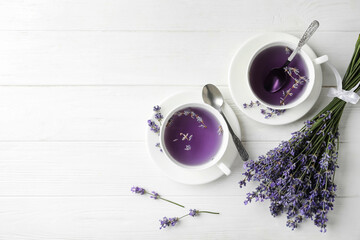 Fresh delicious tea with lavender and beautiful flowers on white wooden table, flat lay. Space for...