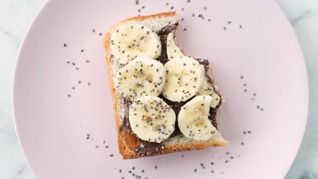 Stop motion animation of food, eating toast with chocolate nut butter, banana slices and chia seeds. Pink background. Healthy school breakfast food concept