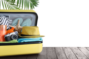 Open suitcase with different beach objects on wooden table against white background. Space for text