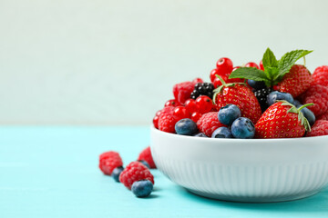 Mix of different fresh berries and mint in bowl on light blue wooden table. Space for text