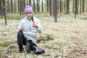 Naklejka na ściany i meble Contented girl with knife and mushroom boletus in hands in pine forest on an autumn day.