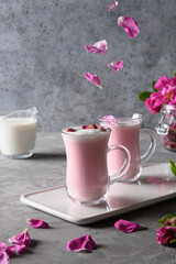 Rose moon milk in glass cups and falling rose petals on grey background. Close up.