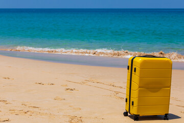 Yellow tourist suitcase on the beach near the blue water.
