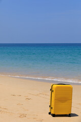 Yellow tourist suitcase on the beach near the blue water.