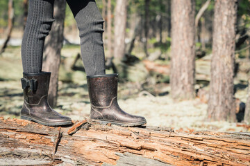 The girls thin legs in rubber boots cross the forest through fallen tree on camping trip.