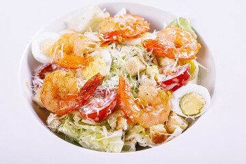 Caesar salad with fried shrimps and parmesan cheese on a white plate. Close-up.