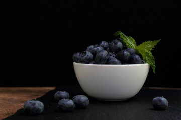 Blueberries with mint leaves in a small white bowl. On a black granite board. Yummy.