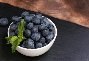 Blueberries with mint leaves in a small white bowl. On a black granite board. Yummy.