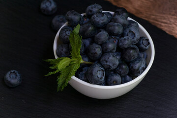 Blueberries with mint leaves in a small white bowl. On a black granite board. Yummy.