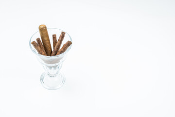Thick cigars from twisted sheets in glass bowl with white background.