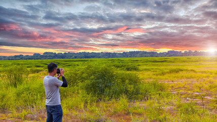 The young man is taking pictures of the beautiful mountain background