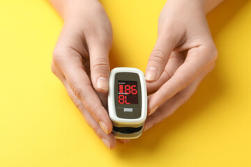 Woman holding fingertip pulse oximeter on yellow background, closeup