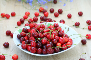 Beautiful red cherry berries in a white plate on the background of scattered on the table