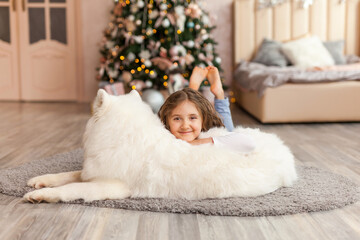 Christmas Child girl with dog Samoyed. New Year at home