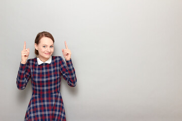 Happy pretty blond girl is pointing with fingers upwards at copy space