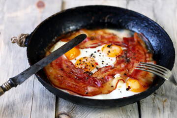 Selective focus. Eggs with bacon in a frying pan. Rustic style. Traditional English breakfast. Keto Diet - An appetizing keto lunch. Fried bacon and eggs.
