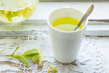 Linden flowers tea in a white cup with silver spoon on a white napkin, on a wooden background,...