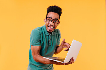 Blithesome student in green t-shirt posing with laptop. Indoor photo of amazed male freelancer...