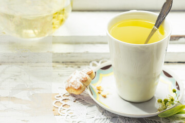 Linden flowers tea in a white cup with silver spoon on a white napkin, on a wooden background and cookie nearby, yellow drink of linden flower on a vintage background, healthcare and healthy eating co